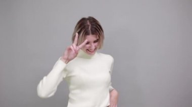 Gülümseyen, zafer işareti ve dil gösteren güzel, komik bir kadın.