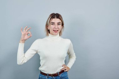 Genç bir kadın işaret işareti gösteriyor, mutlu görünüyor ve gülümsüyor.