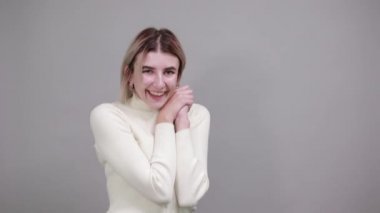 Beyaz elbiseli, gülümseyen genç bir kadın ellerini kaldırarak poz veriyor.