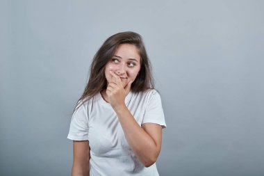 İzole edilmiş duvarın üzerinde beyaz tişörtlü genç bayan avucunu ağzının yanında tutuyor.