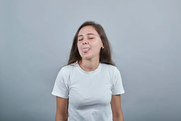 Tiener in wit t-shirt toont haar tong in grap. Gils ziet er kinderachtig en winderig uit. — Stockfoto