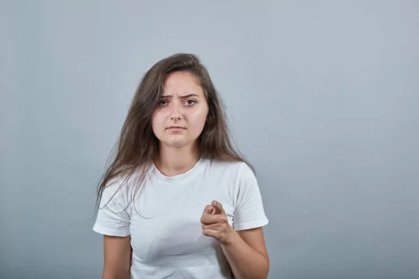 길고 긴 머리를 가진 여자가 격리 된 회색 벽에 실망하여 앞쪽을 가리키고 있다 — 스톡 사진