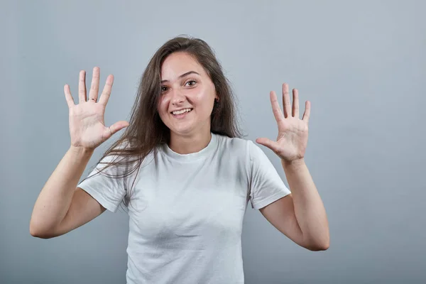 Beyaz tişörtlü kadın gri duvarın üstünde parmaklarıyla on tane sayıyor ve gülümsüyor.. — Stok fotoğraf