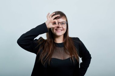 Beyaz tenli güzel bir kadın gözünün yanında işaret işareti gösteriyor, gözlük gibi.