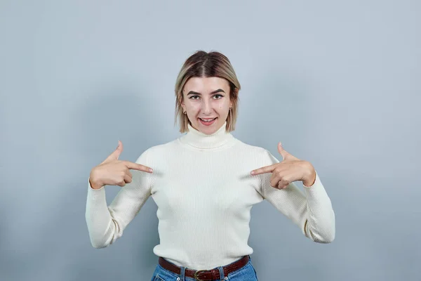 Porträtt av ung kvinna i pastell tröja visar fingrar på bröstet — Stockfoto