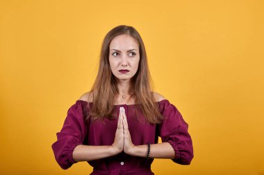 Turuncu duvarın ilerisindeki kişi avuç içlerini bir arada tutar. Af dileyen kişi