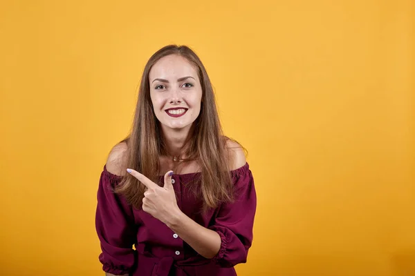 Jovem senhora em borgonha bluse sobre isolado laranja parede apontando dedo para a esquerda — Fotografia de Stock