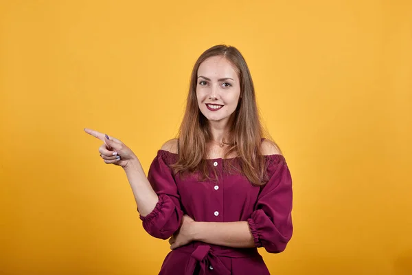Jovencita en blusa color burdeos sobre pared anaranjada aislada apuntando dedo a la izquierda — Foto de Stock