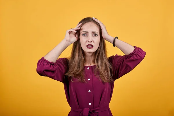 Frau vor orangefarbenem Hintergrund hält Hände auf dem Kopf mit müdem und krankem Gesichtsausdruck — Stockfoto