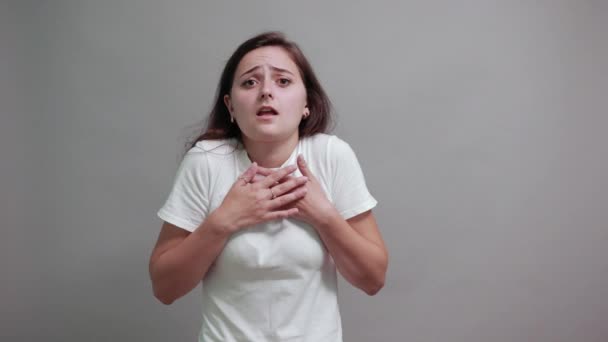 Scared woman in white shirt pointing finger aside, keeping hand on chest — ストック動画