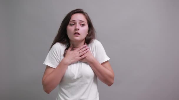 Verrast vrouw in wit shirt houdt hand op borst, wijzende vinger opzij — Stockvideo