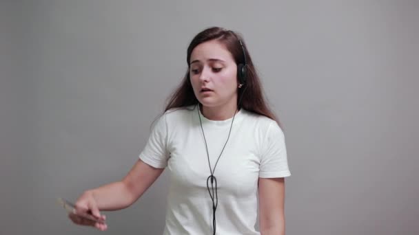 Mujer impactada manteniendo el teléfono, con auriculares bonitos, boca cubierta con la mano — Vídeo de stock