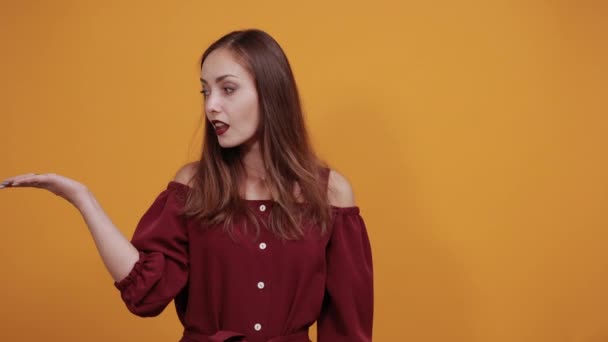Привлекательная брюнетка в бордовом платье поднимает плечи, протягивает руки — стоковое видео