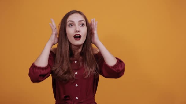 Förvånad kvinna i maroon klänning hålla händerna på huvudet, korrigerar frisyr. — Stockvideo