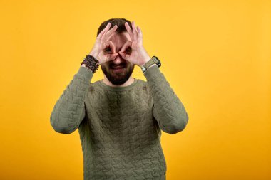 Turuncu duvarın üzerinden neşeli bir adam el ele tutuşuyor, gözler, gözlük hareketi yapıyor.