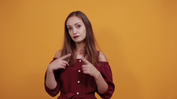 Mujer en vestido granate mirando directamente, manteniendo los dedos en las mejillas, sonriendo — Vídeos de Stock