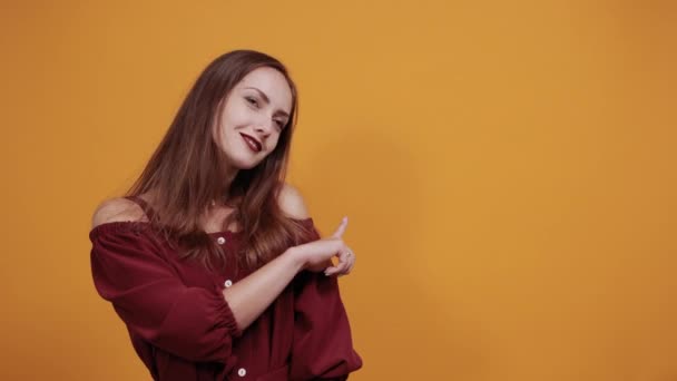 Attractive brunette woman in maroon dress smiling, pointing fingers aside — Stock Video