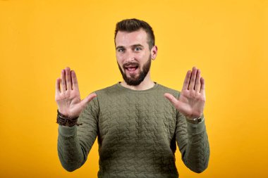 Yakışıklı beyaz adam kameraya avuçlarını gösteriyor, ağzını kapalı tutuyor.