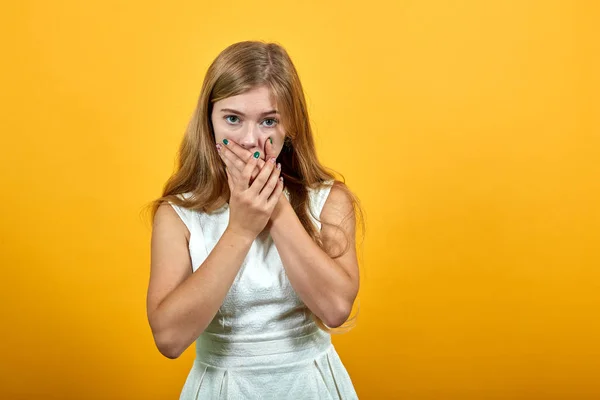 Scared young woman covering mouth with hands, looking frightened.