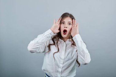 Şok olmuş bir kadın, ağzı açık bir şekilde el ele tutuşup kameraya bakıyor.