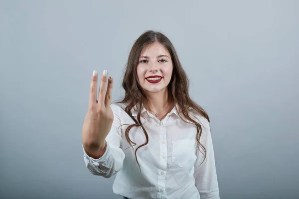 하얀 셔츠를 입고 카메라 앞에 세 손가락을 내보이는 매력적 인 여성, 행복해 보이는 모습 — 스톡 사진