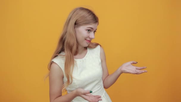 Disappointed blonde young lady spreads hands, looking aside over orange wall — Stock Video