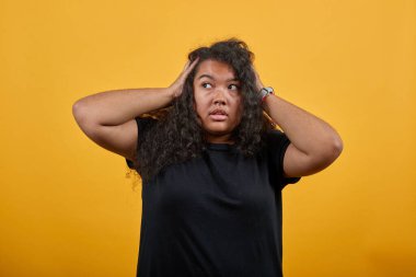 Şok olmuş Afro-Amerikalı genç bir kadın ellerini başının üstünde tutuyor, saçını düzeltiyor..