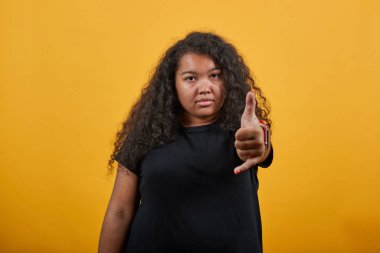 Aşırı kilolu, kameraya başparmak gösteren ciddi bir genç kadın.