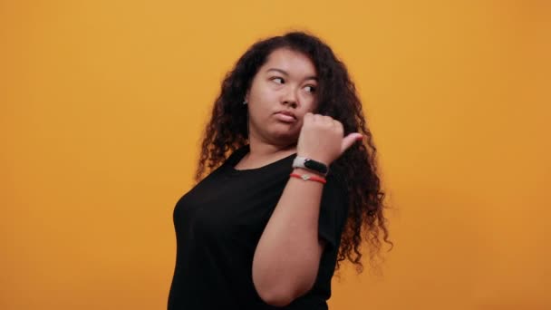 Attraktive afroamerikanische junge Frau zeigt Daumen zur Seite und blickt zurück. — Stockvideo