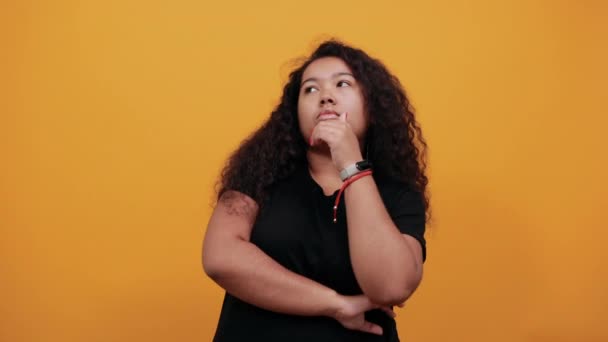Afroamerikanische junge lockige Frau hält die Hand am Kinn, blickt auf, denkt nach — Stockvideo