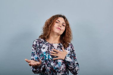 Kadın kendini işaret ediyor, kameraya avuç içi gösteriyor, başını kaldırıyor.