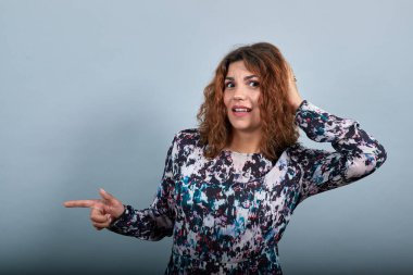 Mutsuz kadın elini başının üstünde tutuyor, doğrudan bakıyor, işaret ediyor..