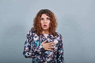 Şok olmuş bir kadın eli göğsünde, ağzı açık, kafası karışmış görünüyor.