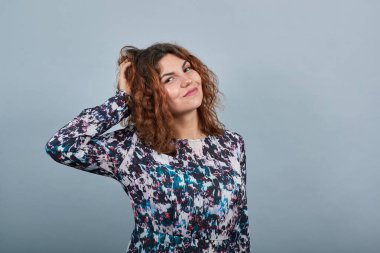 Neşeli bir bayan ellerini başının üstünde tutuyor, doğrudan bakıyor, saç kesimini düzeltiyor..