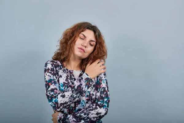 Charming caucasian young woman hugging herself with closed eyes, looking calm