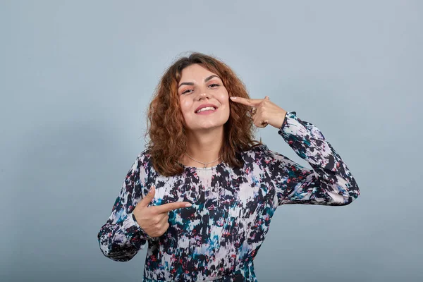 Fröhliche kaukasische junge Frau zeigt mit dem Finger auf Wangen, sieht glücklich aus, lächelt — Stockfoto