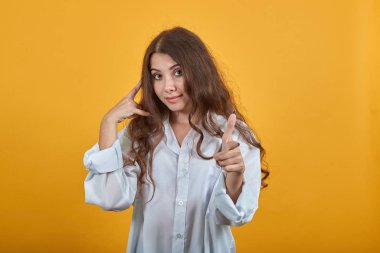 Cep telefonu hareketi yapan, kamerayı işaret eden, doğrudan bakan bir kadın.