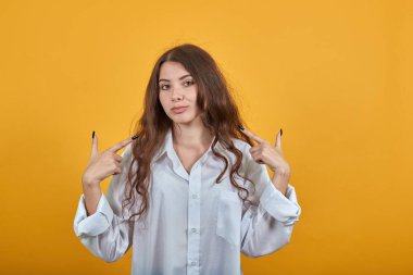 Moda tişörtlü neşeli genç bir kadın gülümsüyor, parmaklarını yanaklarına gösteriyor.