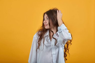 Kıvırcık saçlı kadın ellerini başının üstünde tutuyor, yana bakıyor, güzel bir saç kesimi var.