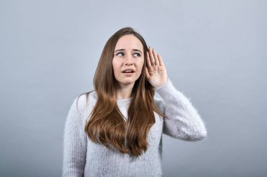 Odaklanmış beyaz kadın elini kulağına koyup dinliyor..