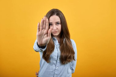 Kafkasyalı esmer kadın kameraya avuç içi gösteriyor, dur hareketi yapıyor.