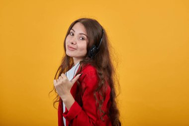 Neşeli genç bir kadın başparmaklarını yana uzatıyor, yan yan bakıyor.