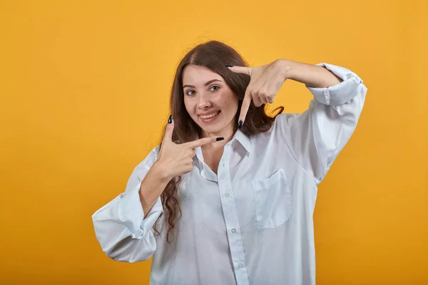 Verrast vrouw in wit shirt doen frame gebaar, glimlachen, kijken naar de camera — Stockfoto