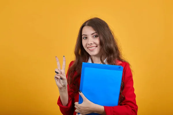 Cheerful woman doing victory gesture, keeping blue folder, looking at camera — 스톡 사진