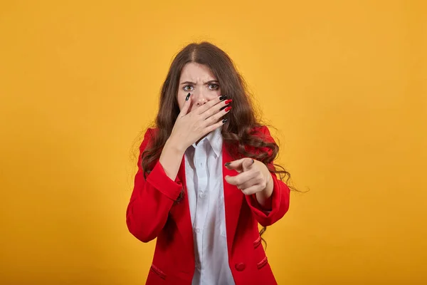 Geschokt vrouw in wit shirt bedekte mond met de hand, wijzende vinger naar de camera — Stockfoto