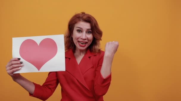 Fröhliche junge Frau, die weiße Leerstellen mit rosa Herz hält und in die Kamera schaut — Stockvideo