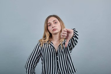 Kafkasyalı genç bir kadın kameraya bakıyor, başparmağını aşağı gösteriyor, mutsuz.