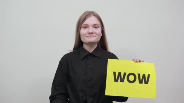 Счастливая очаровательная блондинка держит рекламную бумагу WOW с желтой стеной — стоковое видео