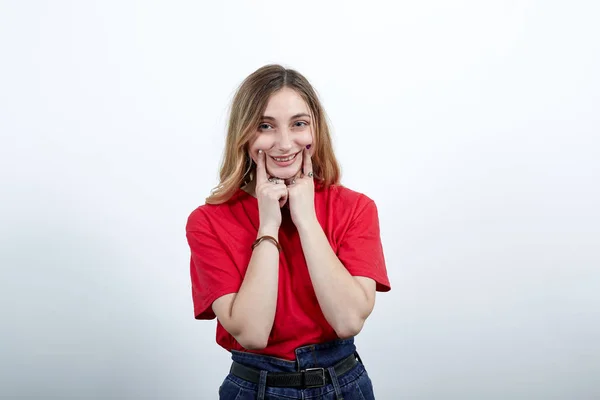 Mulher alegre na moda camisa vermelha sorrindo, mantendo os dedos nas bochechas — Fotografia de Stock