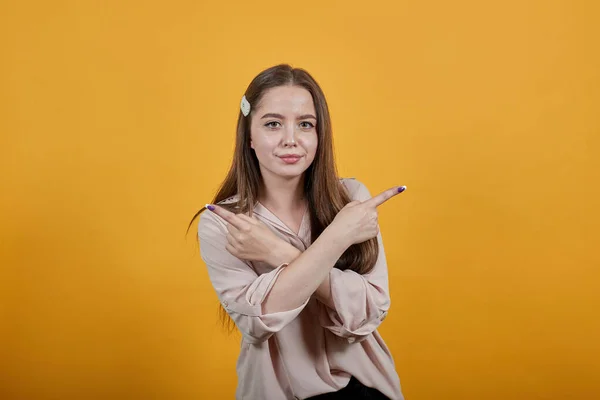 Atractiva mujer en camisa pastel manteniendo las manos cruzadas, señalando con los dedos a un lado — Foto de Stock